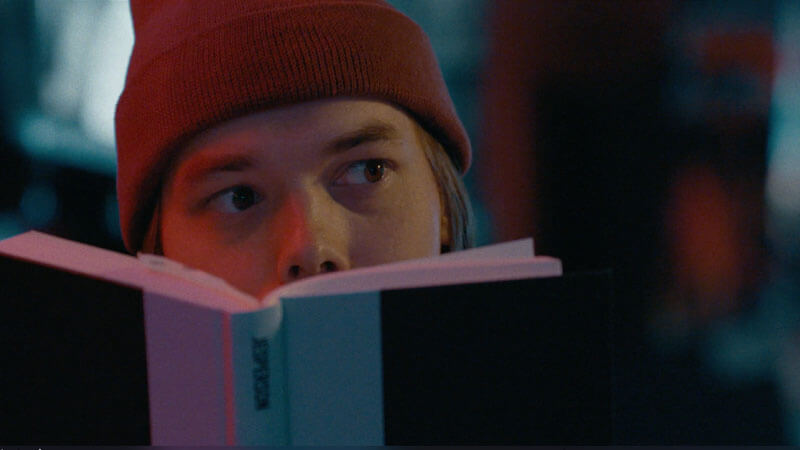 Still from I Will Dare video showing man looking over his book in a bar
