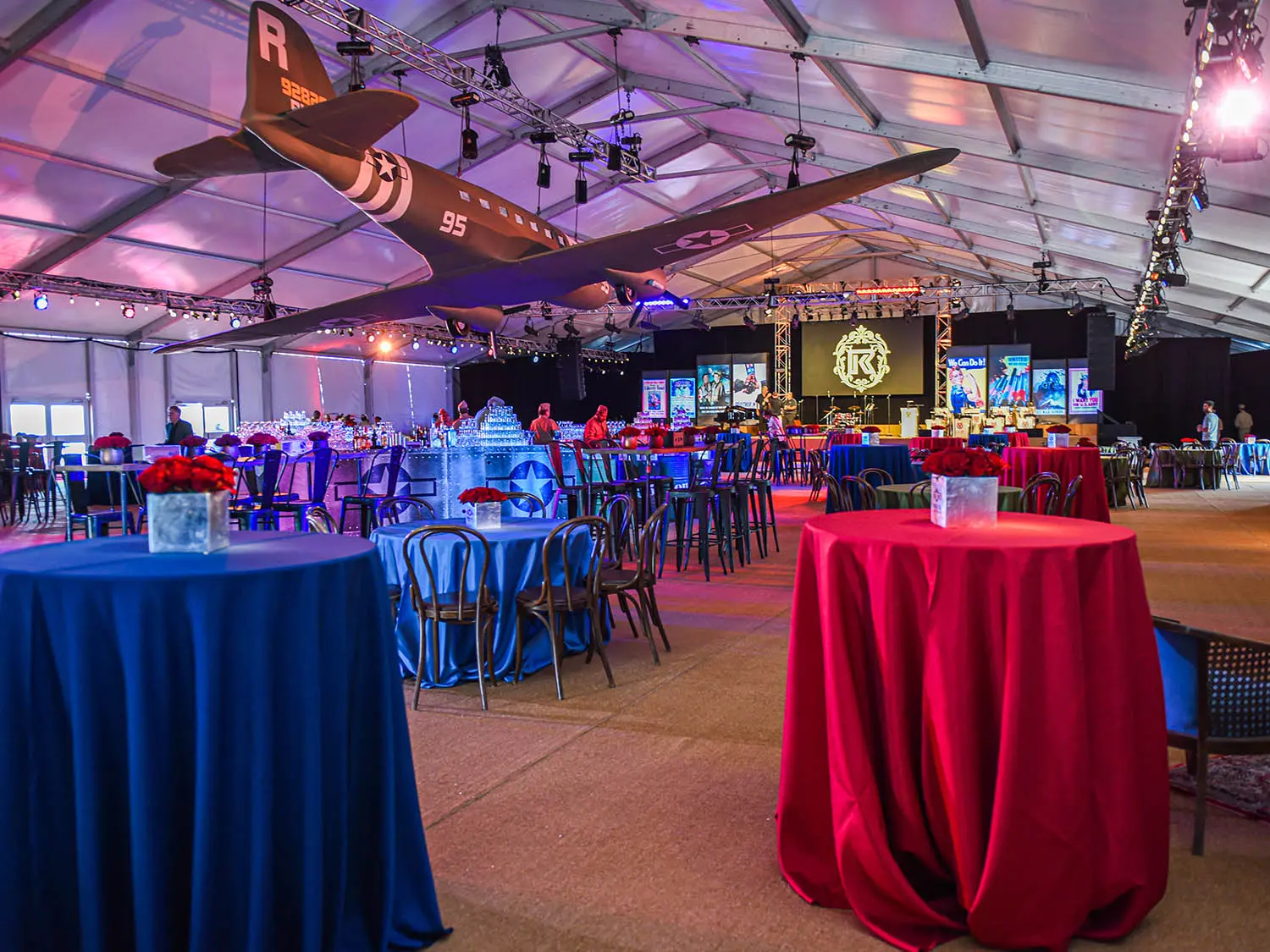 Big tent set up with tables and chairs for event, ww2 plane model suspended from ceiling