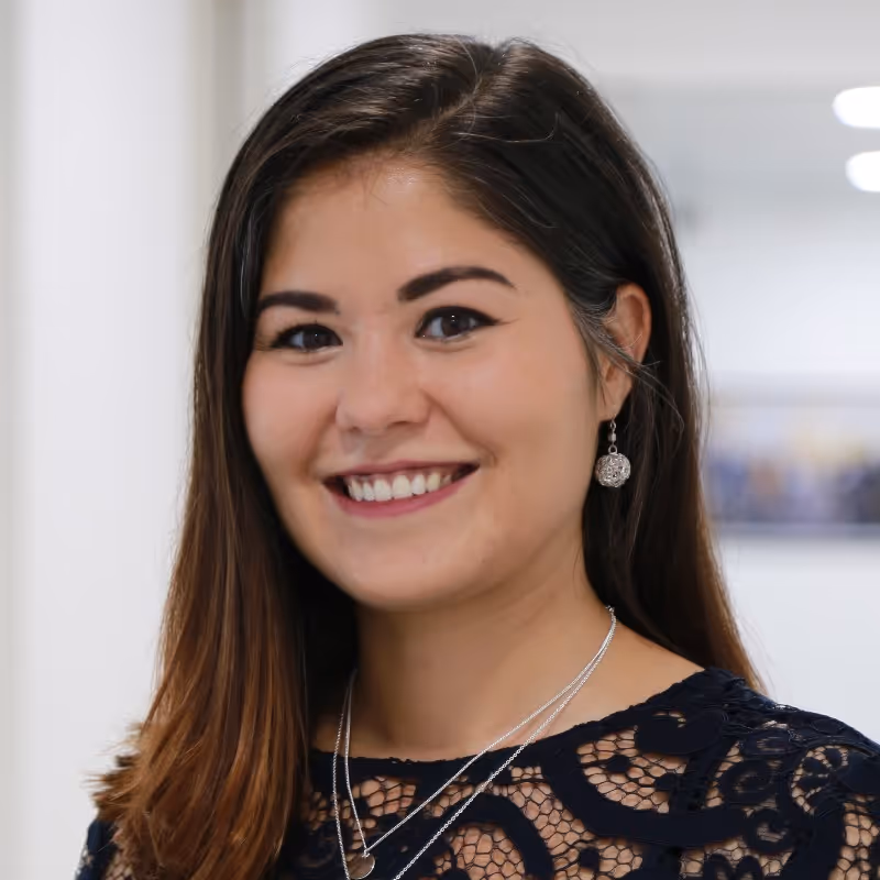 Smiling woman with long brown hair wearing a navy blue lace top, silver earrings, and layered silver necklaces.