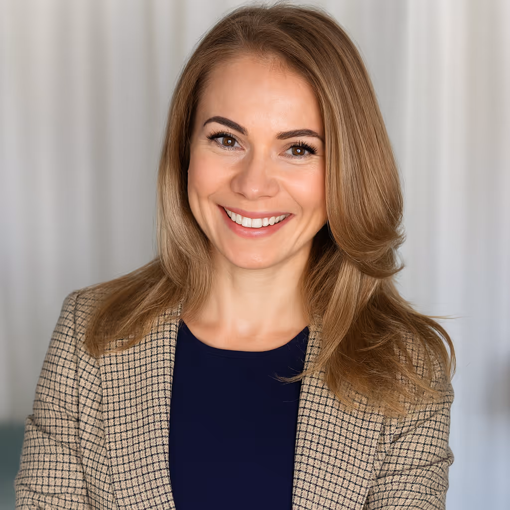 Smiling woman with shoulder-length blonde hair wearing a navy top and checked blazer in front of a light-colored curtain.