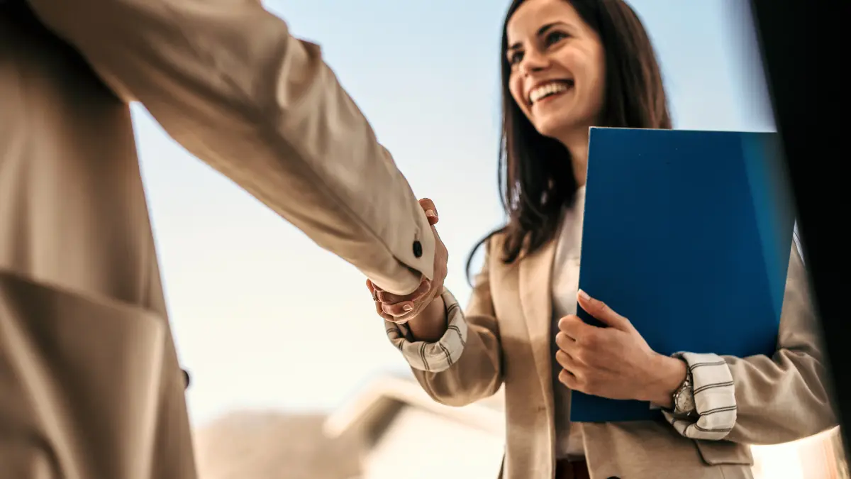 Smiling professional woman holding a folder and shaking hands with a colleague, symbolizing a successful, values-aligned hiring decision.
