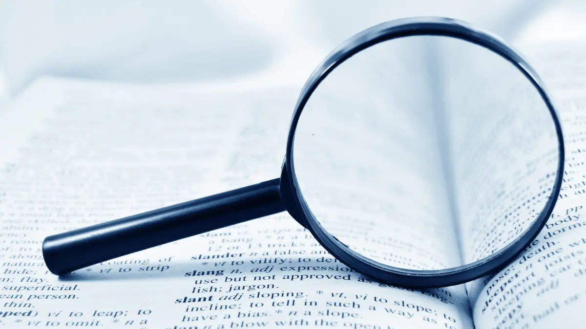 A magnifying glass over dictionary text, symbolizing how employees often need extra help to make sense of confusing benefits jargon.