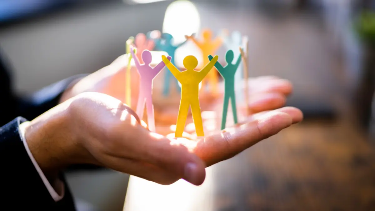 Hands holding a circle of colorful paper cutouts representing people, symbolizing transformational leadership, connection, and inclusive team culture.