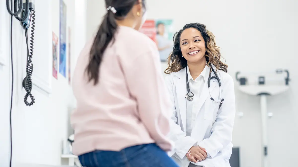 A smiling doctor talks with a patient in an exam room, symbolizing how HR leaders can support preventive care by helping employees access routine screenings and regular checkups.