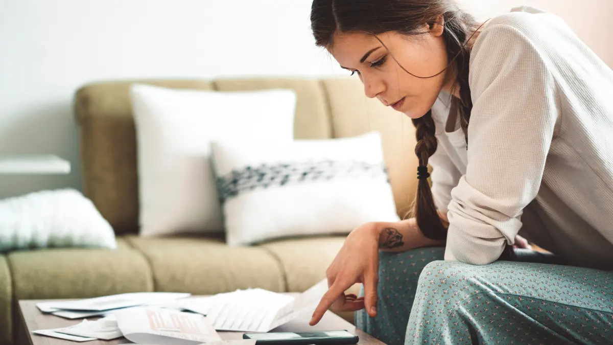 A woman sits on her couch reviewing bills and using a calculator, representing the financial strain of rising healthcare costs.