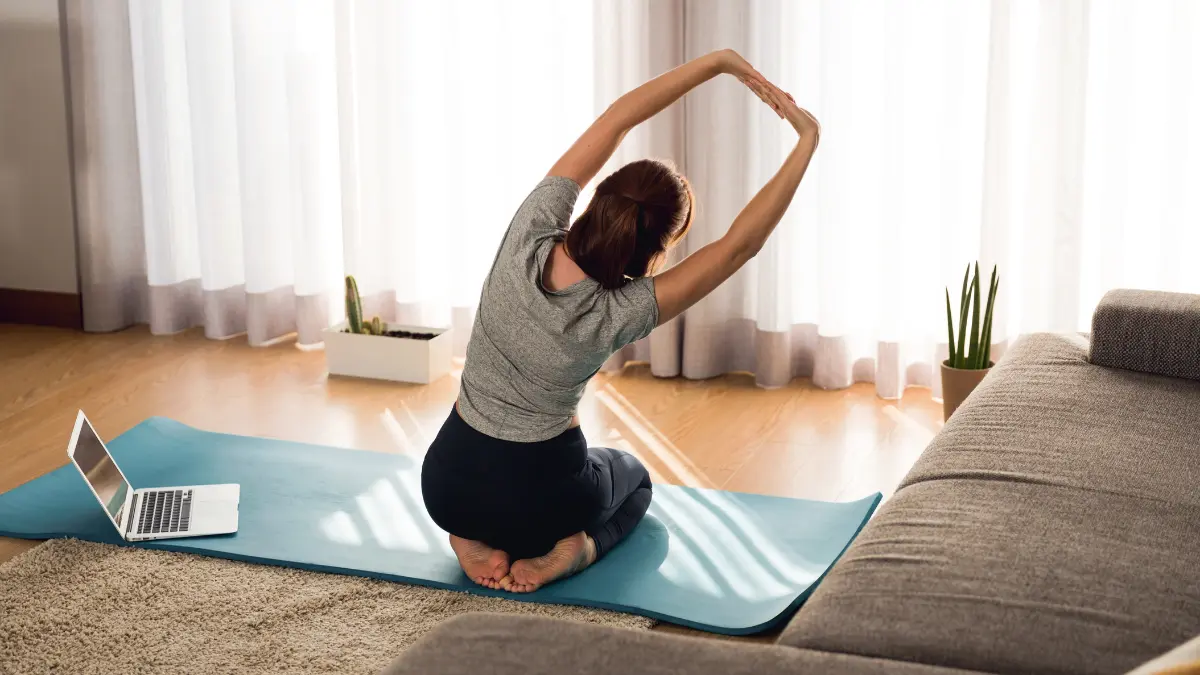 Woman stretching on yoga mat in her room, representing the flexibility that lifestyle spending accounts (LSA) can grant employees when it comes to wellness on their own terms.