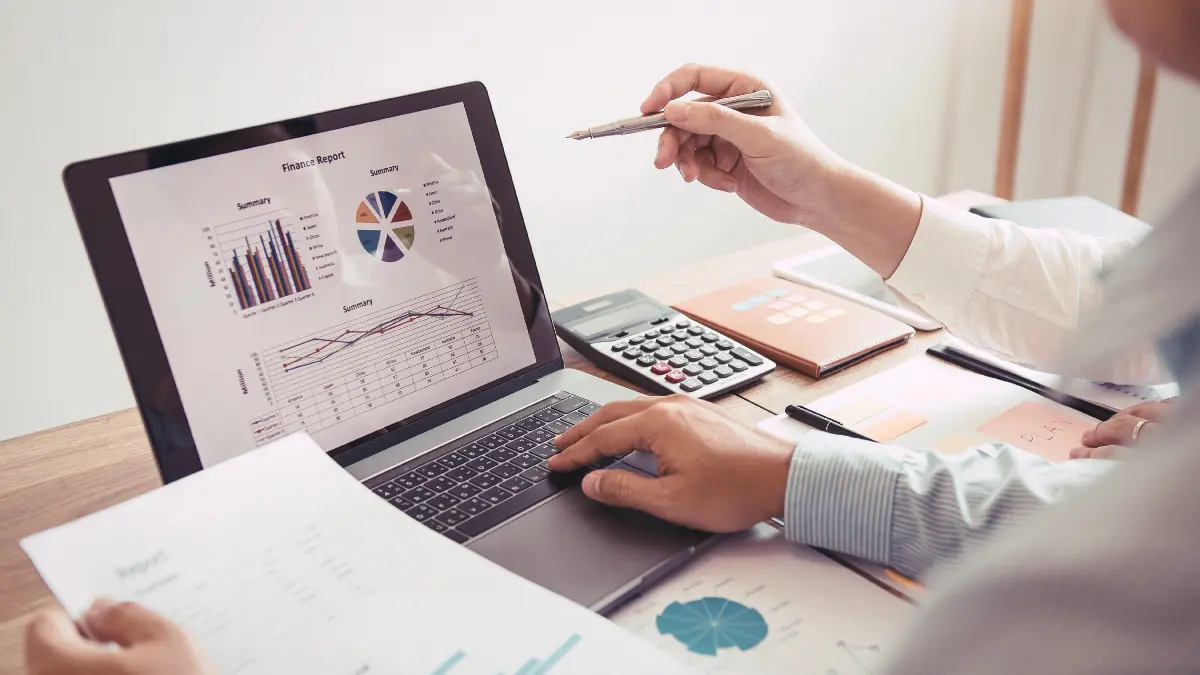 Two professionals reviewing financial charts and reports on a laptop, representing employer health plan claims data analysis