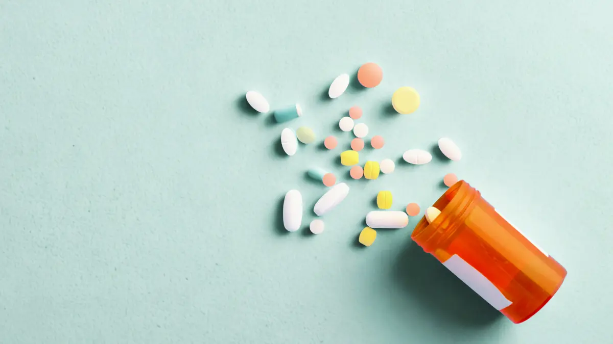 Assorted prescription medications spilling from an orange pill bottle, illustrating pharmacy benefit management and drug cost transparency for employer health plans.