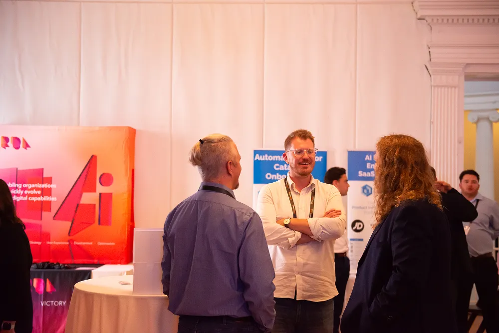Attendees network and chat near sponsor booths at the HawkSearch Customer Summit 25 expo area.