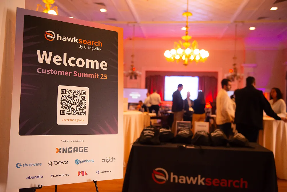 The HawkSearch Customer Summit 25 welcome area featuring branded signage, sponsor logos, and check-in tables.