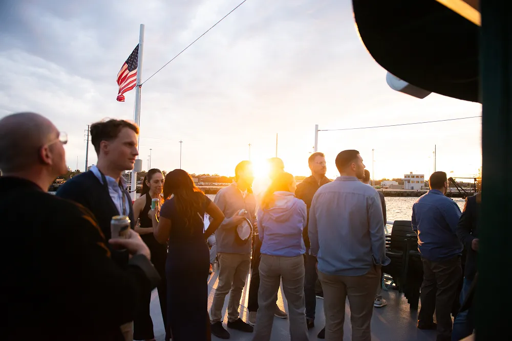 Attendees enjoy a sunset networking cruise during the HawkSearch Customer Summit 25, with an American flag waving in the background.