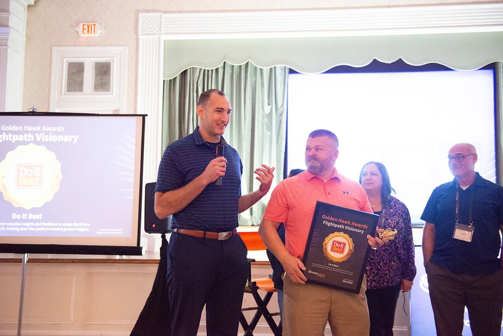 A representative from Do it Best accepts the Golden Hawk “Flightpath Visionary” Award on stage at the HawkSearch Customer Summit 25.