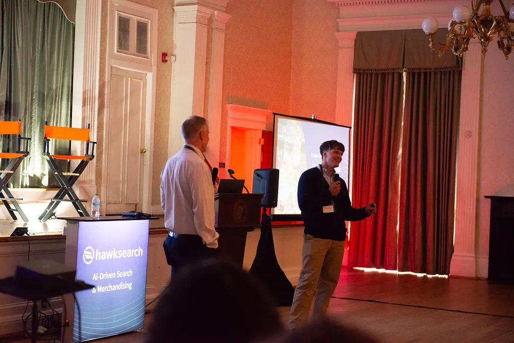 John Murcott and Jordan Coffland share insights at the HawkSearch Customer Summit 25, speaking beside a display reading “AI-Driven Search & Merchandising.”