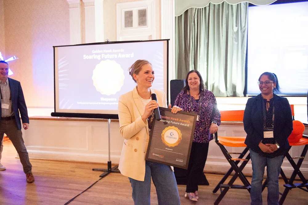 A representative from Shopware smiles while accepting the Golden Hawk “Soaring Future” Award on stage at the HawkSearch Customer Summit 25.