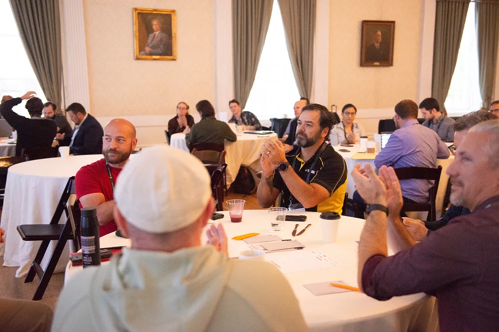 Attendees seated at round tables applaud a speaker during a morning session at the HawkSearch Customer Summit 25.