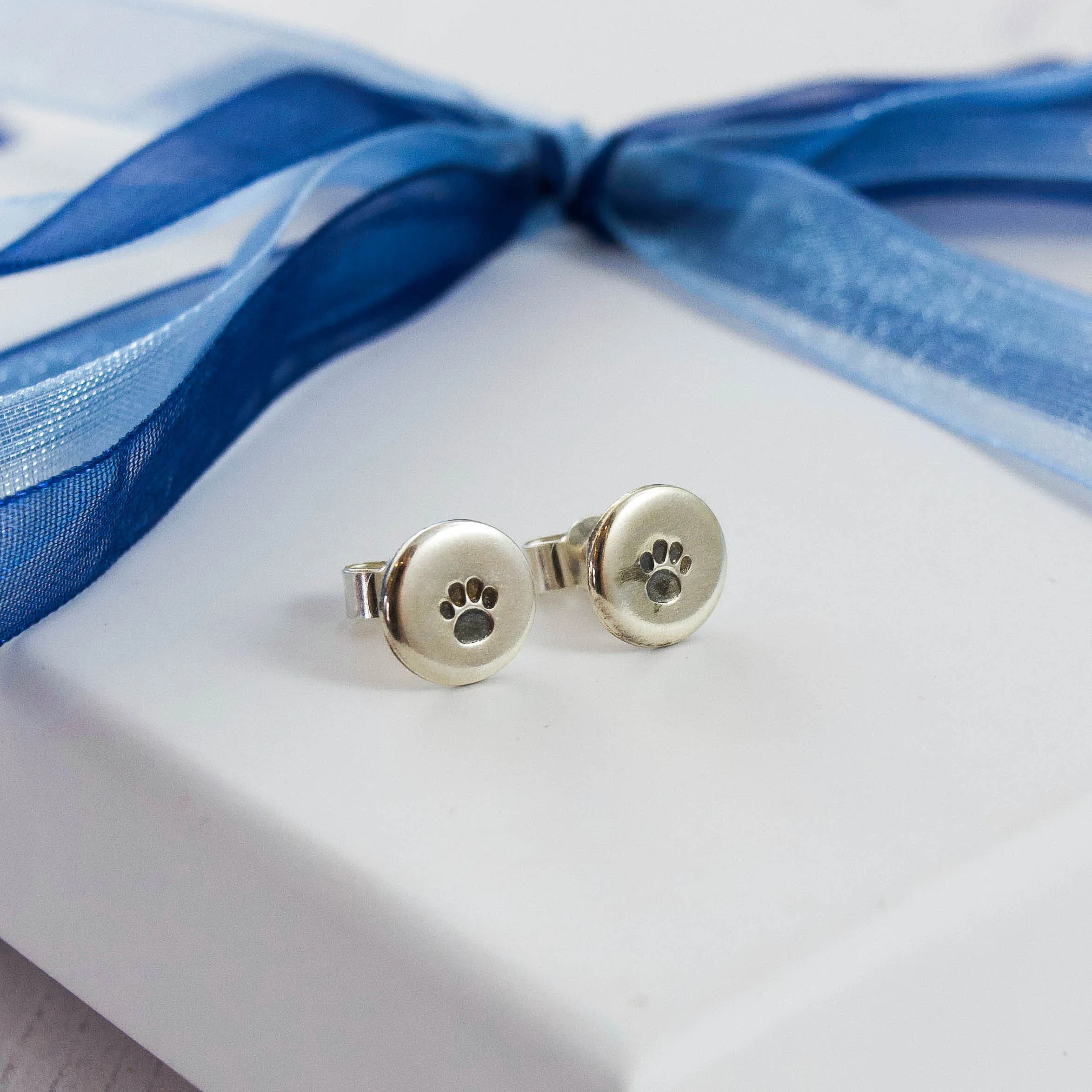 silver disk stud earrings with stamped paw print designhammered texture on white jewellery box tied with blue ribbon
