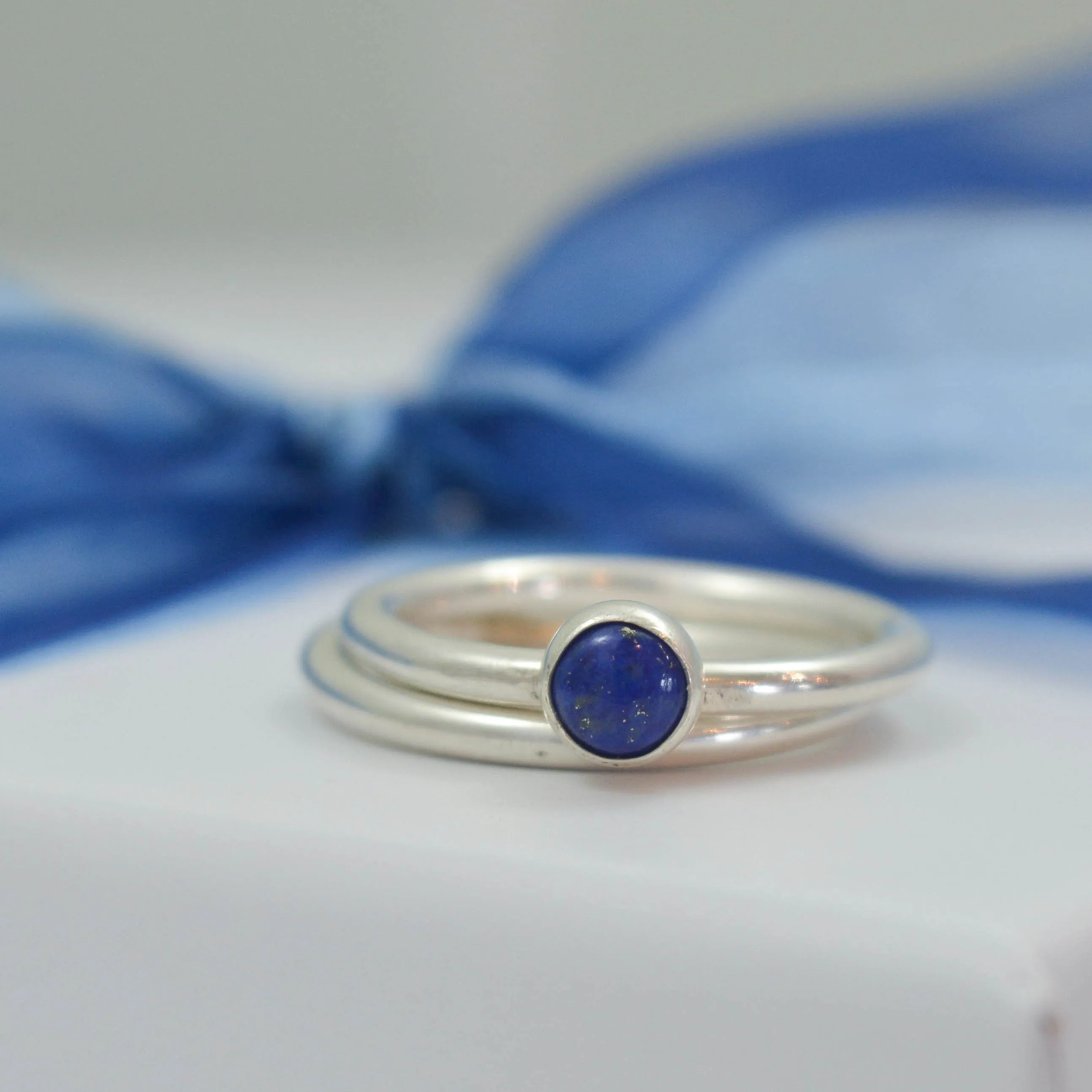 lapis lazuli gemstone ring and silver spacer ring resting on white jewellery box tied with navy blue ribbon