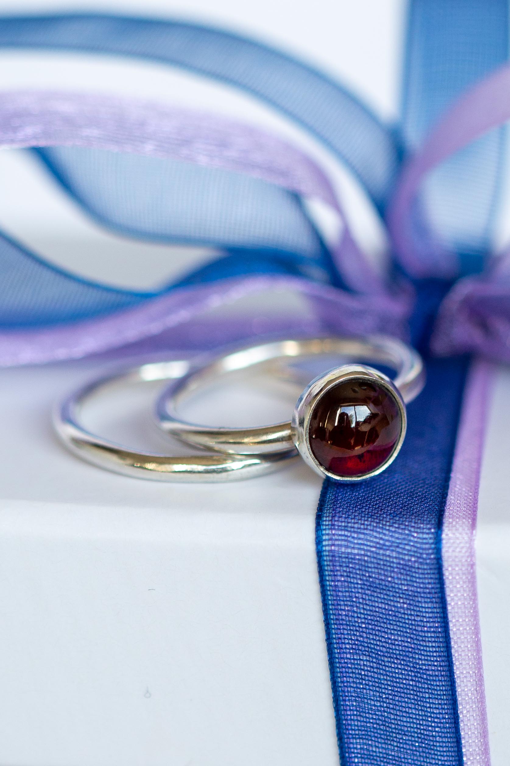 garnet gemstone ring and smooth stacking ring resting on a white jewellery box with navy blue ribbon
