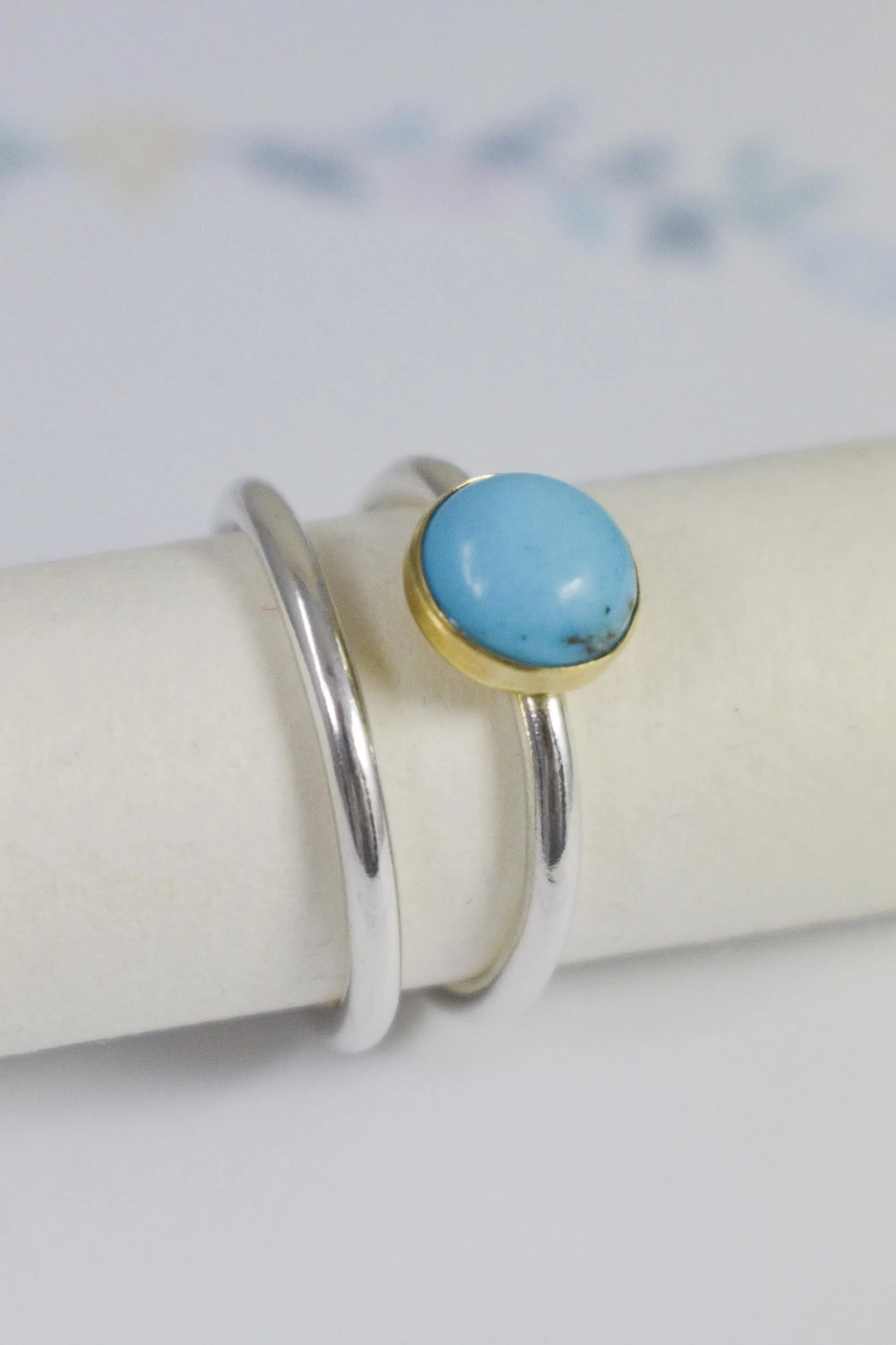 turquoise gemstone ring in gold bezel with silver ring shank and silver spacer ring resting on gift card with floral logo