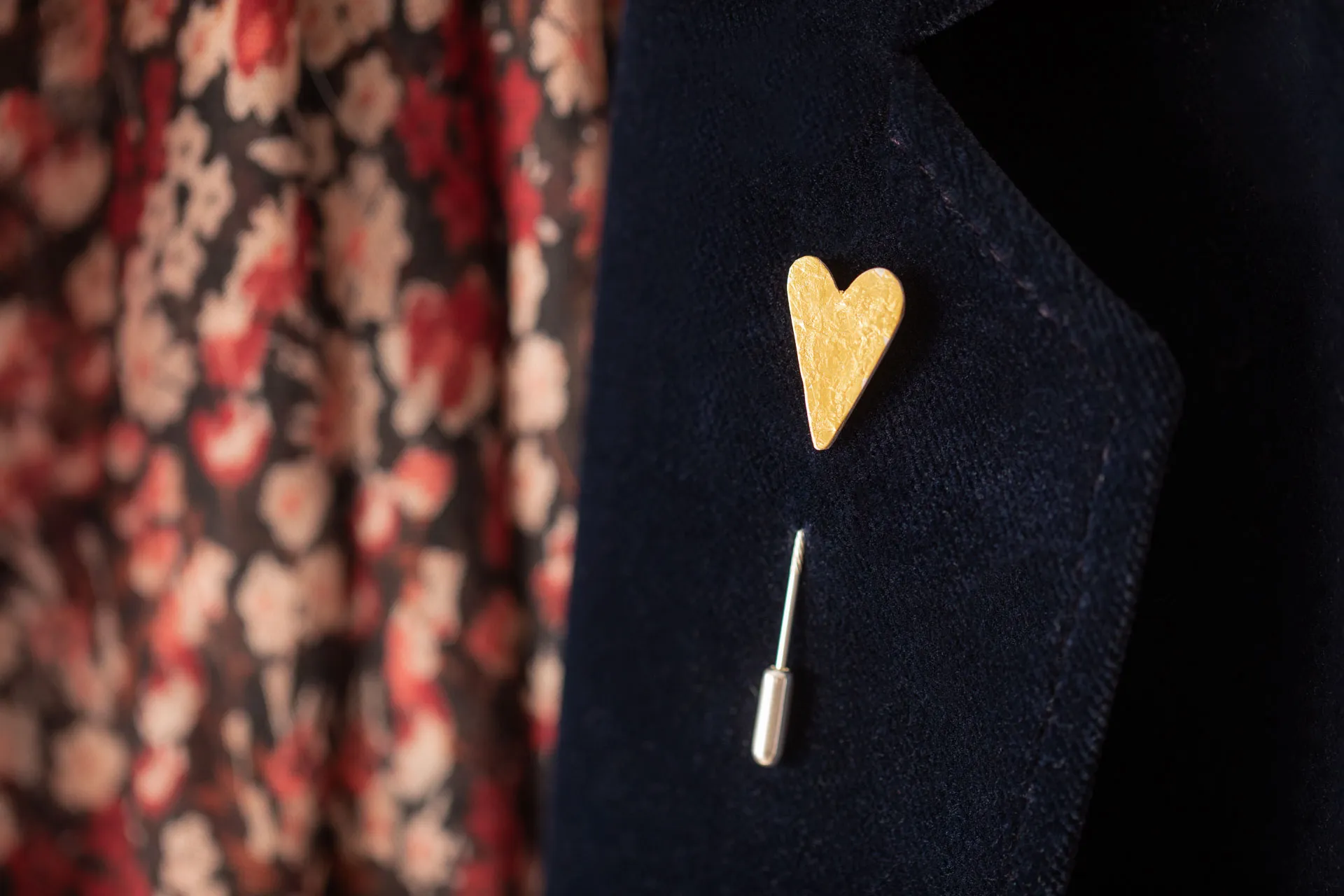 golden hearted pin badge on lapel of dark blue jacket with red floral scarf in background
