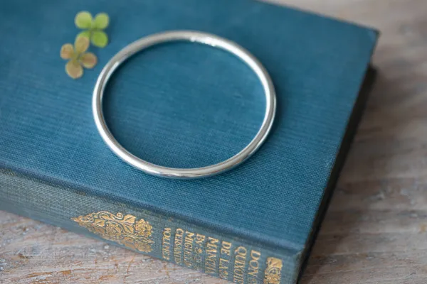 simplicity bangle on dark blue vintage book on pale wooden table with some little flowers in the background