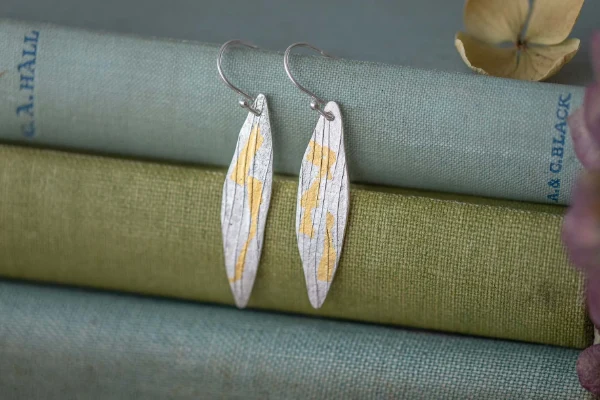willow leaf shaped drop earrings on a pile of books with petals in background 