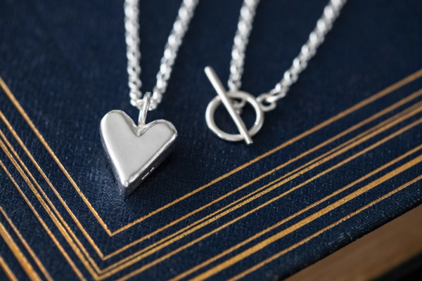 sterling silver highland heart necklace and t bar clasp resting on dark blue book with gold detailing in art deco style
