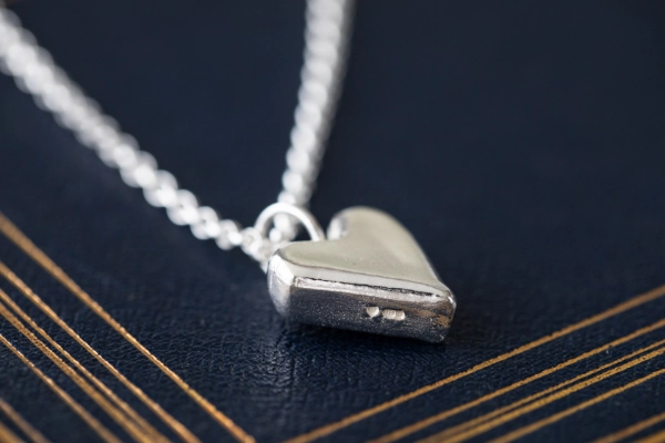 sterling silver highland heart necklace showing hallmark  resting on dark blue book with gold detailing in art deco style