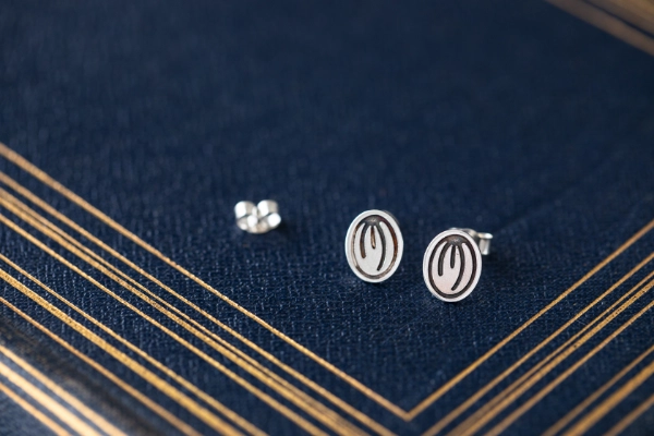 first light silver stud earrings resting on dark blue book with gold detailing 