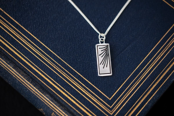 silver art deco inspired necklace resting on dark blue book with gold detailing