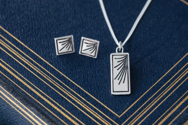 silver stud earrings and necklace with art deco style rays resting on dark blue book with gold detailing