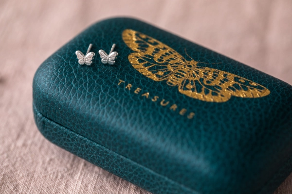 teal jewellery box with gold embossed butterfly with small silver butterfly stud earrings resting on pink tablecloth