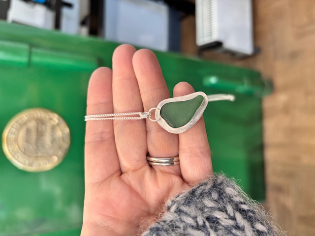 student's sea glass pendant using yellow sea glass with green shop safe in background