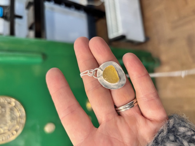 student's sea glass pendant using yellow sea glass with green shop safe in background