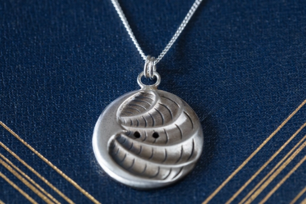 arc and line pendant with button holes and wave texture resting on navy blue vintage book with gold design