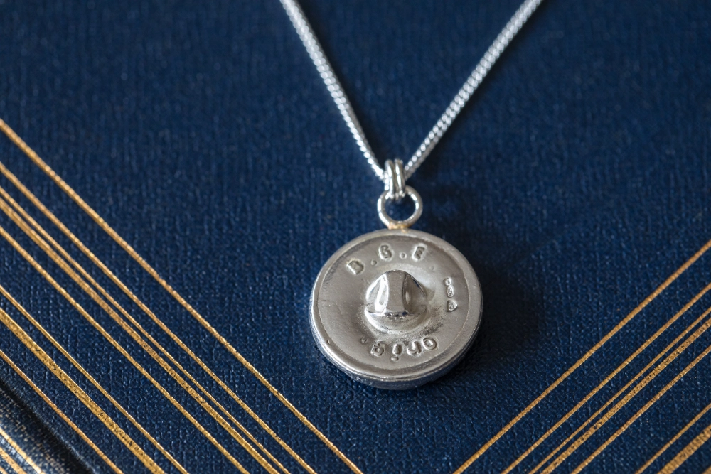 Whispering feather necklace showing button fastening on the back resting on vintage blue book with gold detailing