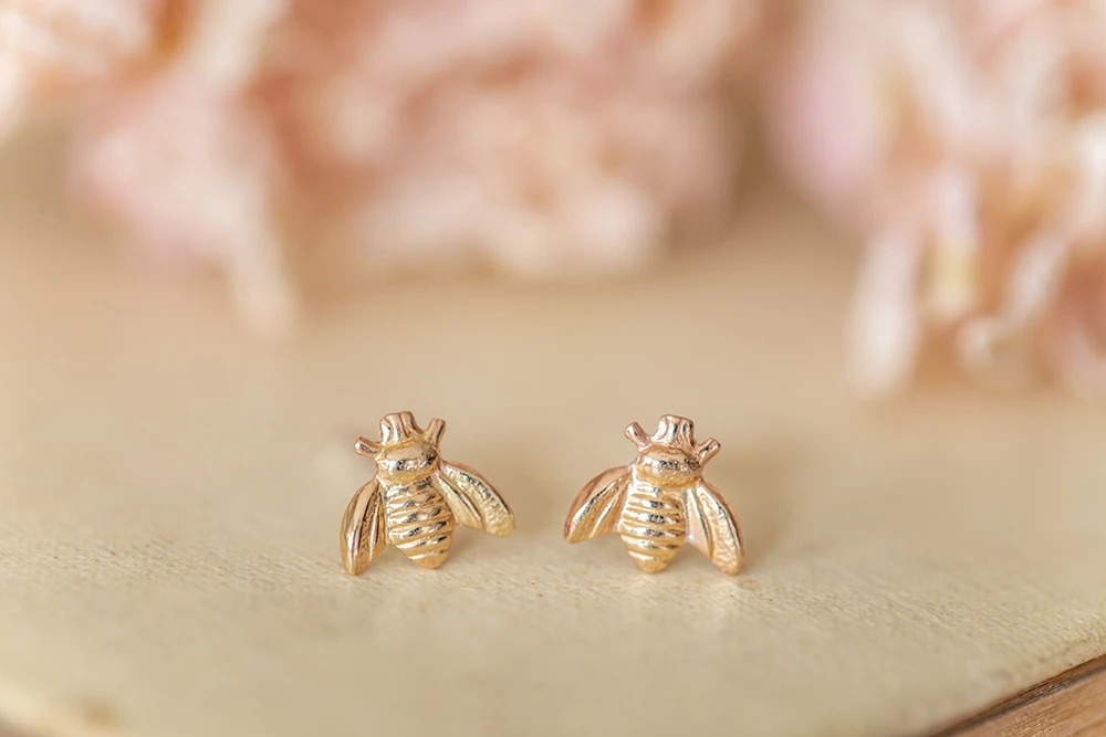 Tiny golden bee studs on sterling silver posts with scrolls—handmade in North Norfolk and perfect as a thank you or birthday treat for a friend or mum.
