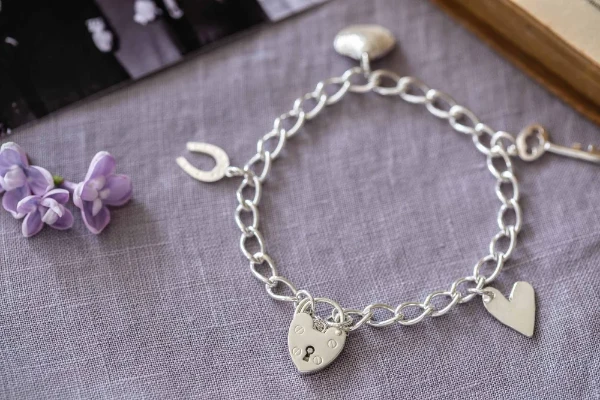 Sterling silver charm bracelet with lock, horseshoe, key, shell, and heart charms. A nostalgic piece celebrating love, luck, and treasured memories.