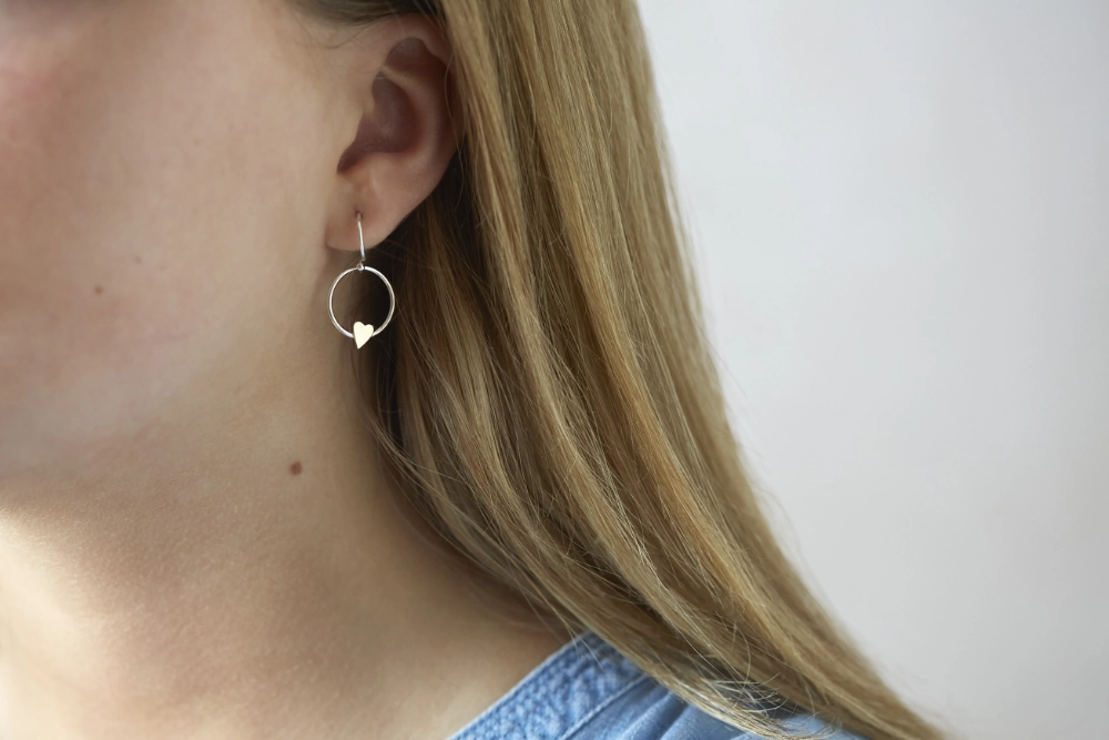 silver hoop drop earrings with a small gold filled heart worn on a woman with long hair 