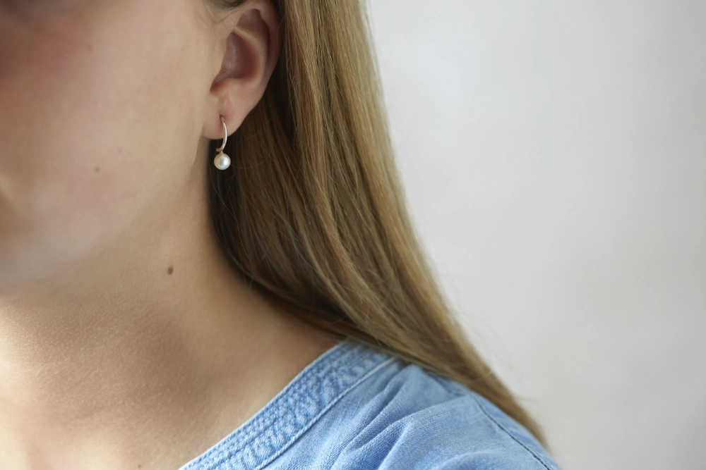 silver hoop earrings with small ivory pearl worn by woman with long hair and blue blouse