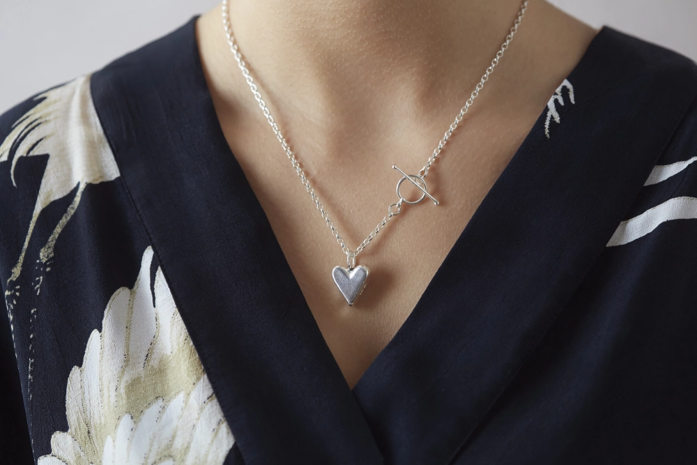 chunky heart necklace with t bar fastening worn by woman in dark black and white blouse
