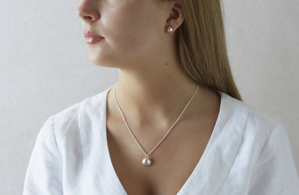 silver cockle shell necklace and stud earrings worn by woman in white linen dress