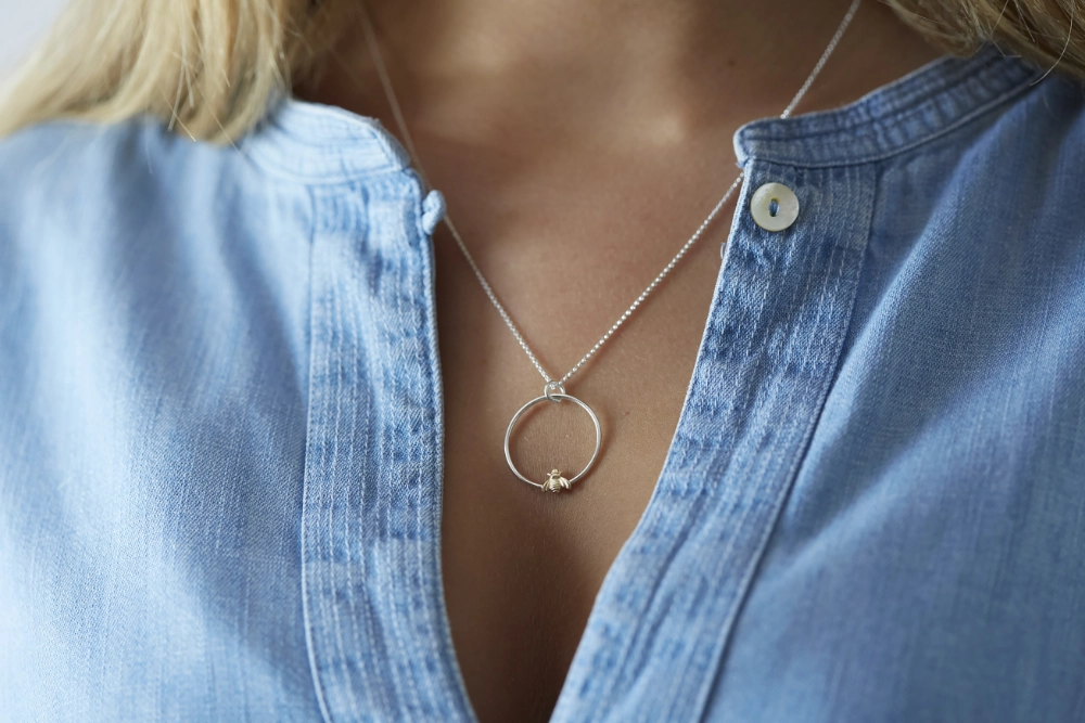 gold bee hoop necklace worn by woman with long hair and a blue denim shirt