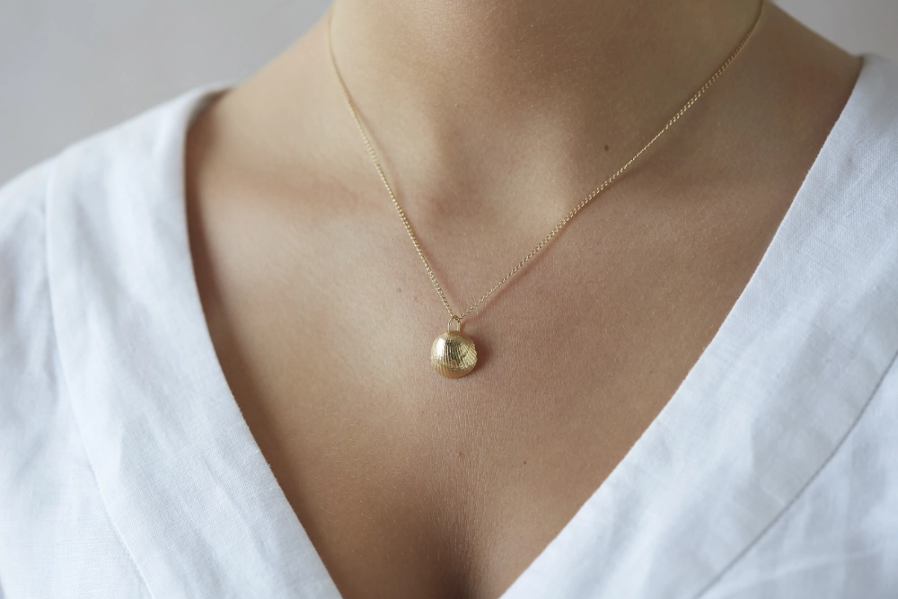 gold cockle shell necklace worn by woman with a white linen dress