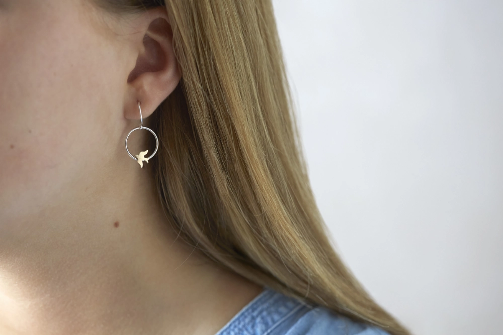 gold swallow hoop earrings worn by woman with long hair and blue denim shirt