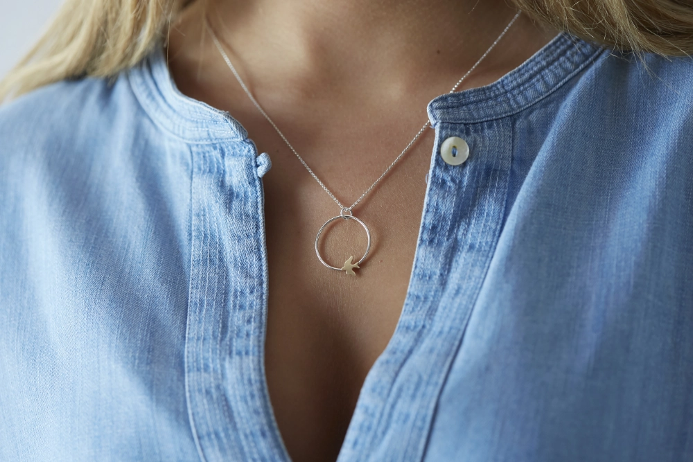 golden swallow hoop necklace worn on woman with long hair and blue denim shirt