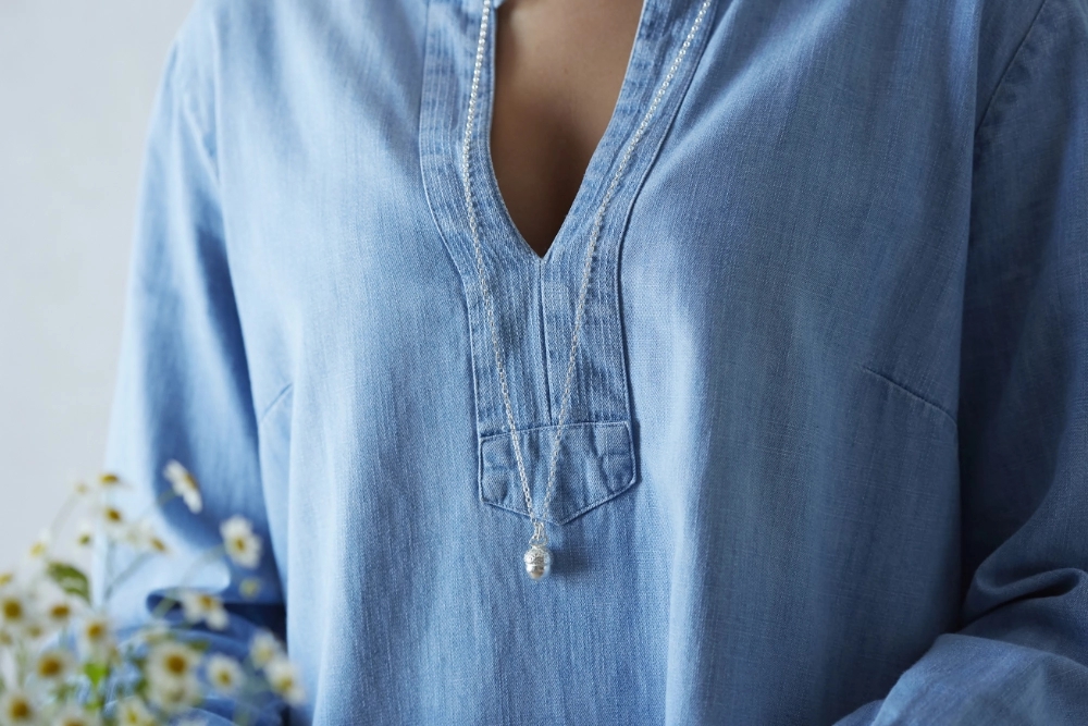 Holkham Acorn silver necklace worn by woman in blue denim shirt holding a bunch of flowers
