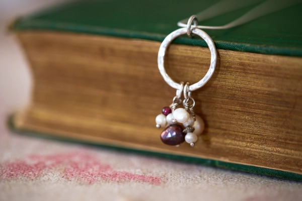 gathered pearl necklace hanging from vintage green book resting on pink and plum vintage tablecloth