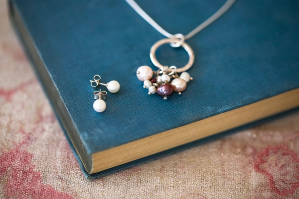 Freshwater pearls white and pink and plum hanging on hammered hoop with chain and ivory pearl studs resting on dark blue book and vintage pink and plum tablecloth