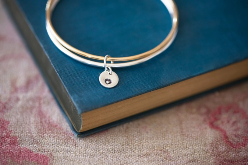 silver and gold filled twinned bangle with added heart charm on vintage blue book